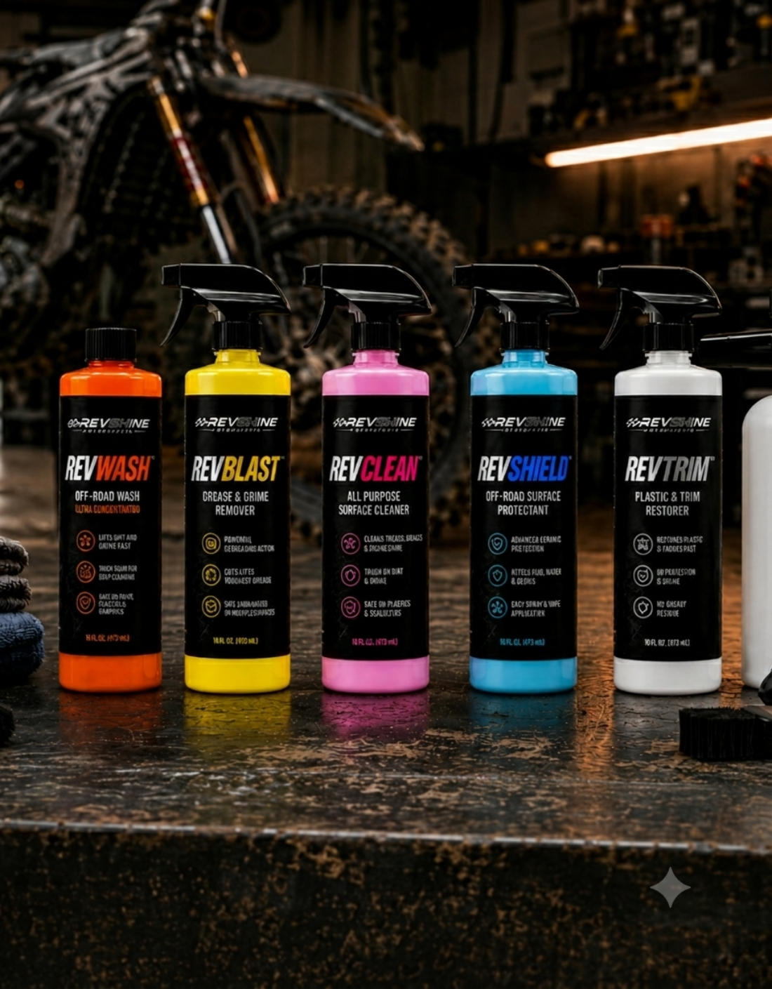 RevShine off-road cleaning product lineup displayed on a workbench, featuring RevWash, RevBlast, RevClean, RevShield, and RevTrim bottles with dirt bikes in the background.